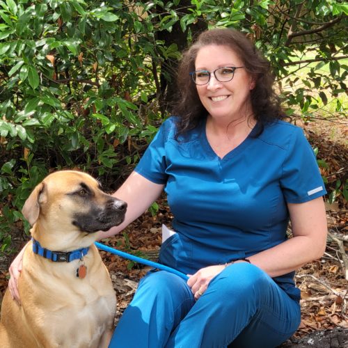 Tania Workman in blue scrubs sitting outside with a tan dog.